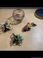 Photo showing three porcelain floral candle holders and one round art glass candle holder on a wooden surface