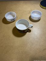 Three small porcelain bowls on a table; two are round with blue floral patterns, and one is a cup-shaped bowl with a handle and colorful design.