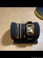 Overall view of the watch and three bracelets on a black foam display stand.
