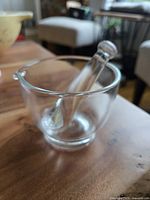 Side view of the clear glass mortar and pestle on a wooden table, showing the pouring spout and rounded shape.