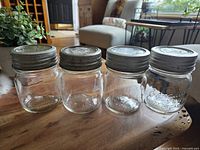Four vintage half pint sealer glass jars with metal zinc screw collars placed on wooden surface in indoor setting.