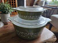 Both vintage Pyrex Spring Blossom casserole dishes stacked together showing lids and side floral pattern in olive green.