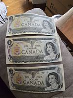 Front side of three vintage 1973 Canadian one dollar banknotes showing portrait of Queen Elizabeth II in grayscale with denomination and bilingual text