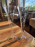 Two vintage Art Nouveau champagne flutes side by side on wooden surface. Clear glass with star etching visible.
