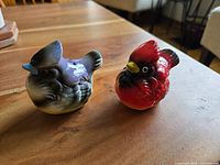 Pair of light blue/gray bluebird and bright red cardinal ceramic bird salt and pepper shakers on wooden table, viewed from side angle.
