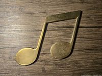 Top down view of vintage brass music note wall hanging showing overall shape and patina on wood surface background
