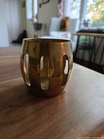 Side view of the brass tealight holder showing vertical cutouts and patina on the surface.