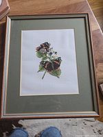 Framed cross-stitch artwork showing two butterflies on leaves with flowers, viewed from the front.