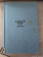 Front cover of the vintage book showing its blue textured surface with a small decorative emblem and some stains.