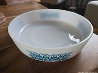 Side view showing turquoise floral decorative pattern on white milk glass round baking dish.