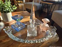 Photo of vintage Fostoria clear glass vanity tray holding three vintage perfume bottles in blue, clear, and pink glass with unique stoppers.