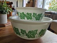 Side view of two stacked vintage Hazel Atlas Ivy pattern milk glass mixing bowls showing green ivy leaf pattern on white glass.