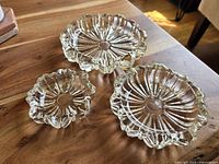 Three vintage Hazel Atlas clear glass nesting ashtrays with fluted Art Deco design, shown separately on wooden table.