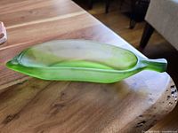 Side angle of green translucent glass banana shaped dish showing length and details of the stem and curves