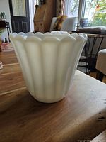 Front side view showing the scalloped edges and fluted vertical grooves of the white milk glass planter on a wooden table.