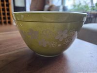 Side view of green Pyrex Crazy Daisy mixing bowl on wooden table showing floral pattern and bowl shape.