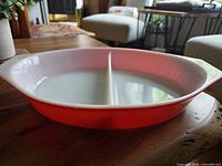 Side angle view of the red divided casserole showing the partition and handles.