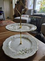 Front view of the 2-tier dessert stand on table showing the floral patterned plates and gold-colored handle.
