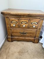 Close-up photo of the nightstand front showing three small panels with white knobs and one larger drawer with brass handle.