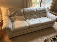 Front view of cream leather sofa with three seat cushions and padded backrests, showing minor wear on the leather surface.