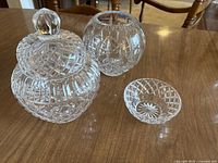 Photo showing three crystal glassware items: a covered jar with knob lid, a medium vase, and a small bowl, all with cut glass diamond patterns.