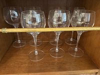 Six large etched crystal wine glasses arranged in a row inside a wooden cabinet.