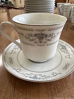 Close-up photo of a white porcelain cup with the matching plate beneath. Both feature blue floral patterns and gold trim.