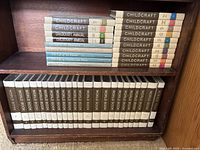 A bookshelf showing multiple Childcraft volumes and a complete set of World Book Encyclopedias arranged in two shelves. The Childcraft books have colored bands with volume numbers visible, including various annual editions.