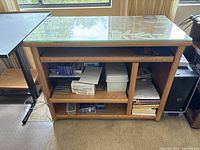 Full view of light brown wooden desk with glass top showing open shelves and storage space beneath, minor surface scratches visible.