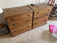 Two brown wooden dressers placed side by side on a carpeted floor, each with three drawers and metal handles. Shows overall look and condition.
