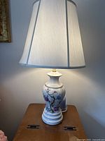 Full view of the lamp with a white fabric lampshade turned on, showing the lamp base on a wooden surface.