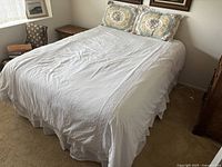 Bed made with white bedspread covering the full mattress, two floral pillow shams visible on top of headboard area.