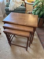 Set of three nested wooden tables with smooth brown finish and turned legs, shown stacked together.