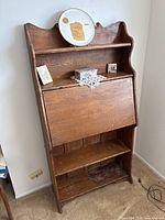 Full front view of the brown wooden drop-front desk showing upper shelf, closed drop-front panel, and lower open shelf.