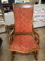 Front view of traditional wooden rocking chair showing patterned fabric seat and backrest, warm brown wood finish, and minor wear.