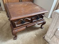 Full view of the wooden side table showing two front drawers with decorative handles and visible surface wear on the tabletop.