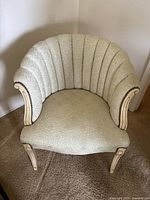 Front view of the beige upholstered chair showing curved back and patterned fabric upholstery with vertical channel tufting.