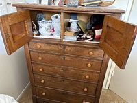 Full frontal view of wooden cabinet with two open upper doors revealing internal storage and four closed drawers below with wooden knobs.