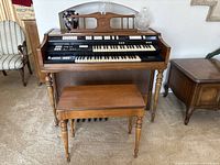Front view of Wurlitzer electric organ, showing one manual keyboard, built-in speakers, and bench in front.