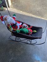 Full view of Santa and mouse figures sitting inside the wicker sleigh on a concrete floor