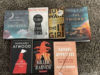 Photo showing all seven paperback books arranged on carpet, titles visible including 'The Dictionary of Dreams,' 'The Turn of the Key,' 'The It Girl,' 'The Thicket,' 'The Handmaid's Tale,' 'Killer Harvest,' and 'Savage Appetites'.