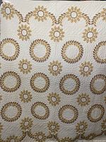 Full view showing the cream background quilt with beige and brown circular floral pattern, highlighting the detailed stitching and overall design.