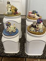 Four white ceramic kitchen canisters with colorful detailed lids featuring kitchen and food-themed 3D ceramic figurines.