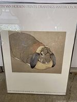 Framed print artwork showing close-up view of rabbit illustration and text including artist name and Oakland Museum retrospective.