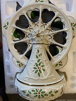 Front view of white ceramic Ferris wheel decoration with holly and berry design on the base and wheel.
