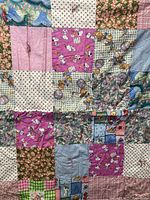Close-up of patchwork quilt showing varied fabric patterns including floral prints, checkered patches, and cartoon dogs on pink background.