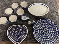 Overview of all Polish pottery items in the lot including bowls, platters, spoon rest, and creamer arranged on carpet.
