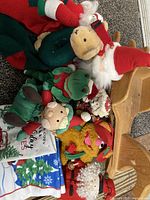 Lot of holiday-themed plush toys, stockings, and wooden rocking horse on carpeted floor