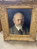 Front view of the oil portrait painting showing an elderly man with glasses, wearing a suit, set in an ornate gold frame with intricate carving.