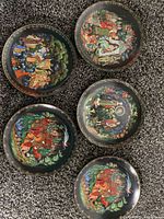 Top view of all five collectible Russian fairy tale plates spread on carpet, showing colorful detailed illustrations on dark backgrounds.